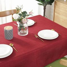 a red table cloth with white plates and flowers in a vase on the table top