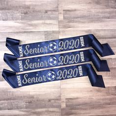 three blue ribbons with the words senior year and soccer on them are laying on a wood floor