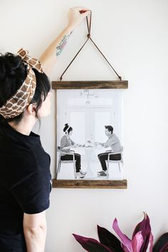 a woman holding up a framed photo hanging on a wall