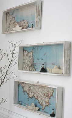 three framed maps hang on the wall above a mantel with a vase and branch