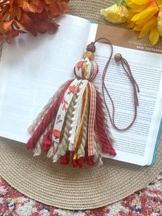 a bookmark with tassels on top of an open book next to flowers