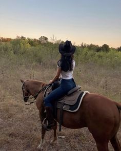 a woman riding on the back of a brown horse in a field next to trees