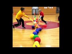 two young boys playing with balls on a basketball court in front of an orange and yellow ball