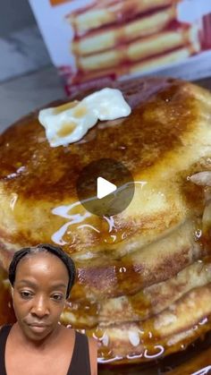 a woman standing in front of a giant stack of pancakes with syrup on it and butter