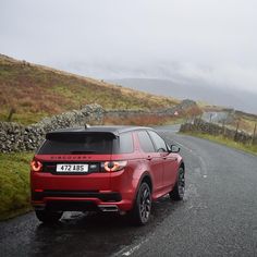 a red range rover driving down a country road