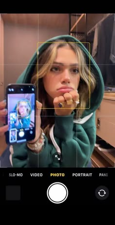 a woman taking a selfie with her cell phone in front of her face while wearing a green hoodie