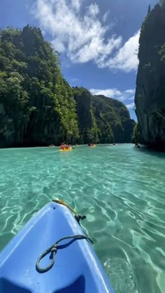 a kayak is in the water near some cliffs and trees, while another boat floats by