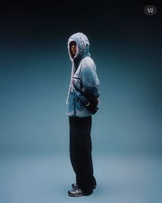 a man standing in front of a blue background wearing a hoodie and black pants