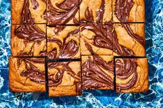 chocolate frosted brownies are arranged in squares on a blue surface with water behind them