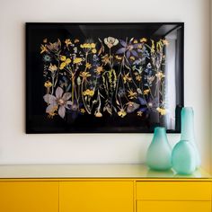 two vases sit on a yellow dresser in front of a black and white painting