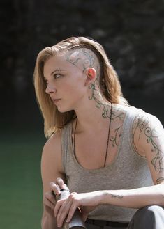 a woman with tattoos on her head and neck sitting next to a water fountain holding a bottle