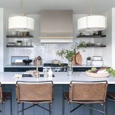 a kitchen with three bar stools in front of an island and two lamps above it