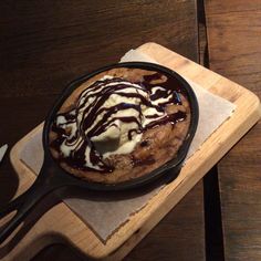 a skillet filled with ice cream and chocolate on top of a wooden cutting board