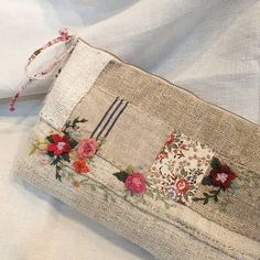 an old purse with flowers on it sitting on top of a white cloth covered surface