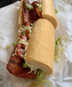 two hotdogs with meat, lettuce and tomatoes on them sitting on wax paper