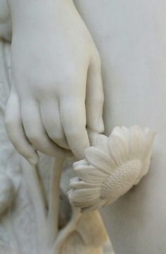 a white statue is holding a flower in it's hand and touching the petals