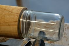 a glass jar sitting on top of a piece of wood next to a wooden handle