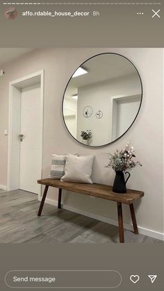 a wooden bench sitting in front of a round mirror on the wall next to a vase with flowers