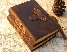 a brown leather book with a bow tie on it sitting next to a pine cone