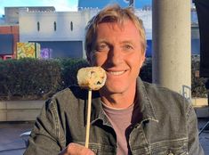 a man is holding up a piece of food on a stick in front of his face