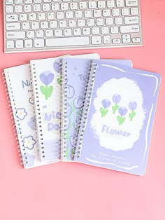 three notebooks sitting next to a keyboard on top of a pink surface with flowers