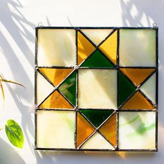 a green and yellow stained glass mosaic on a white wall next to a potted plant