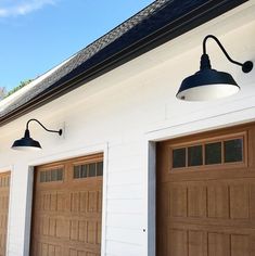 two garage lights on the side of a white building with brown doors and black shingles