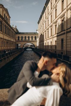 a man and woman kissing on the side of a river in an alleyway near buildings