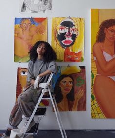 a woman sitting on a stepladder in front of paintings