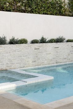 an empty swimming pool in front of a white brick wall and planters on either side