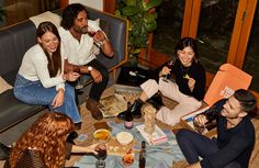 a group of people sitting around a table with drinks and snacks on it, all smiling