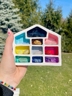 a hand holding a small house made out of different colored paints in it's center