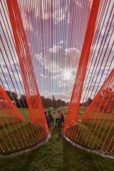 two people are walking through an art installation with orange lines on the ground and grass in front of them