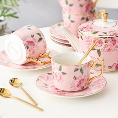 pink and gold tea set with matching saucers, cups and spoons on a white table