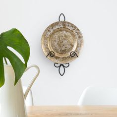 a white vase sitting on top of a wooden table next to a wall mounted plate