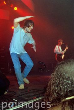 two young men on stage with one holding his arm in the air while another man is playing guitar