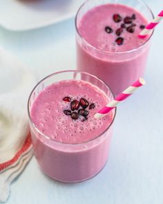 two glasses filled with pink smoothie and topped with pomegranates