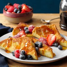 french toast with berries and syrup on a white plate next to a bowl of strawberries