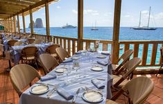 an outdoor dining area overlooking the ocean with tables and chairs covered in blue cloths