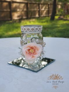 a glass jar with a flower in it on top of a white table cloth covered table