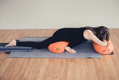 a woman in black shirt doing yoga on blue mat with orange pillow and towel around her