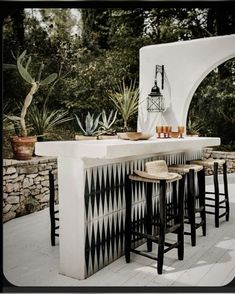 an outdoor kitchen with bar stools and potted plants