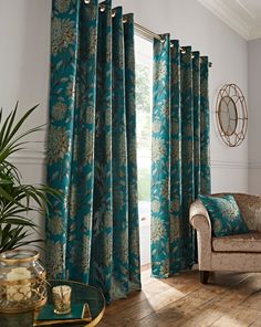 a living room filled with furniture and a window covered in blue floral drapes next to a chair