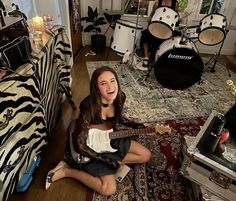 a woman sitting on the floor with a guitar in front of her and other musical instruments behind her