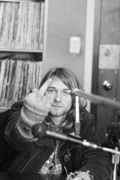 a man sitting in front of a microphone with his hand up to the camera and another person standing behind him