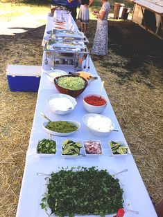 a long table with bowls and plates of food on it, at an outdoor event