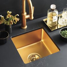 a kitchen sink with gold faucet and black countertop next to it is surrounded by flowers