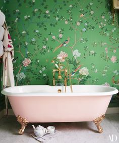 a pink bathtub sitting in front of a green wall with flowers and birds on it