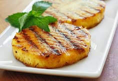 two grilled pineapples on a white plate with green garnishes