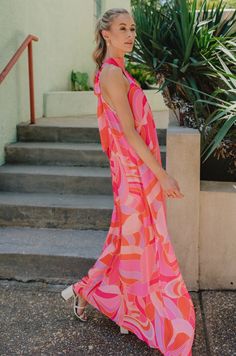 The Josephine Multicolor Printed Halter Maxi Dress is a vibrant and eye-catching garment that exudes summer elegance and playful charm. Its bold color palette of red-orange, pink, and purple creates a stunning visual impact, reminiscent of a tropical sunset or a vivid summer garden in full bloom. Crafted from lightweight fabric, this maxi dress flows effortlessly with every step, offering both comfort and style for warm-weather occasions. The halter neckline of the Josephine dress adds a touch of sophistication while providing support and structure to the silhouette. Its sleeveless design allows for freedom of movement, making it perfect for outdoor events or beachside strolls. A geometric pattern adorns the fabric of the dress, adding depth and visual interest to the overall design. The p Pink Sleeveless Maxi Dress Beach Cover-up, Playful Pink V-neck Dress, Vibrant Sleeveless Maxi Dress With Vibrant Print, Pink Sleeveless Dress With Vibrant Print, Playful Pink Sundress For Vacation, Chic Dresses With Vibrant Print For Summer Parties, Vibrant Print Dresses For Summer Parties, Vibrant Summer Sundress For The Beach, Colorful Maxi Dress For Summer Day Out